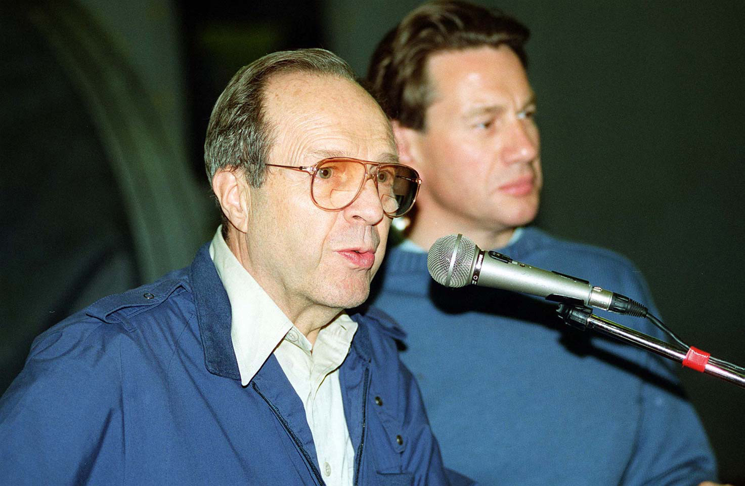 US Defense Secretary William Perry speaking at a microphone with Michael Portillo, UK Secretary of State for Defence, behind him — mid-1990s.