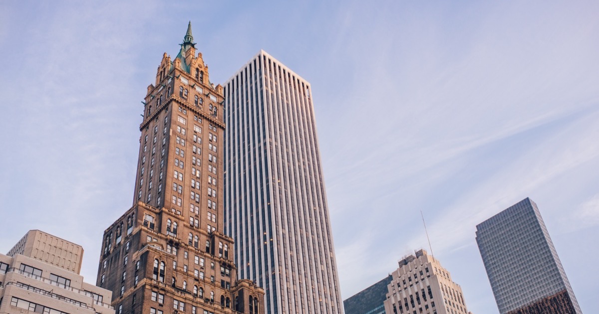 The General Motors Building’s white marble piers rising beside the Sherry-Netherland’s ornate tower, seen from near Central Park in low golden light.