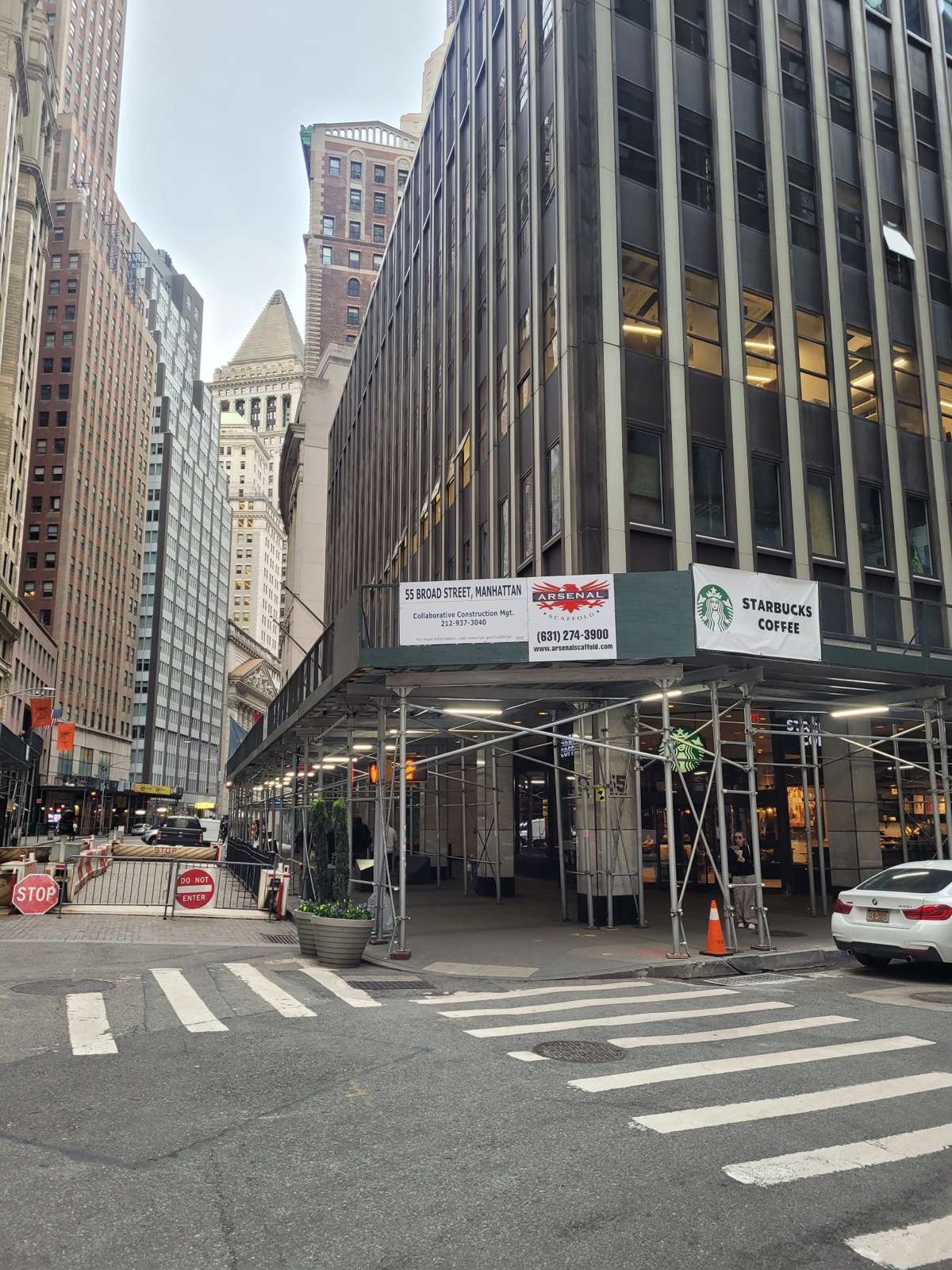 55 Broad Street in 2024, mid-conversion — scaffolding and a construction-management banner at the base of the 1960s tower Goldman Sachs once occupied.