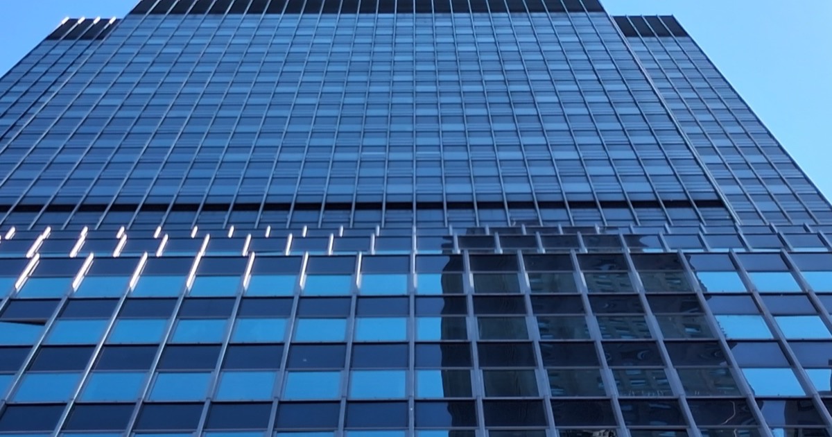 The glass facade of 25 Water Street rising against a blue sky — the re-clad 1969 tower after its conversion to 1,320 apartments.