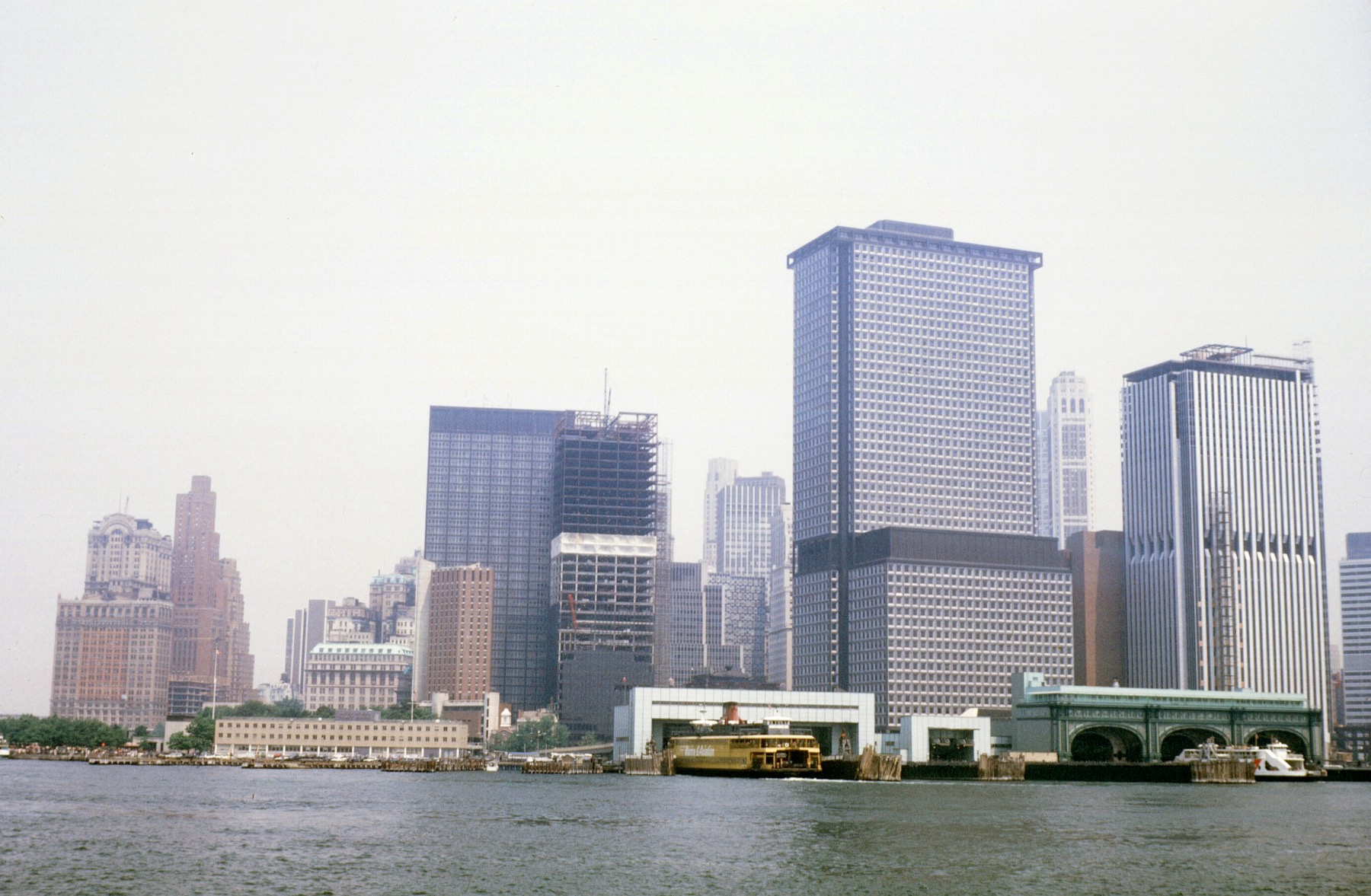 Lower Manhattan from the harbor in the late 1960s — the waterfront office boom under construction, a Staten Island ferry at the slip.