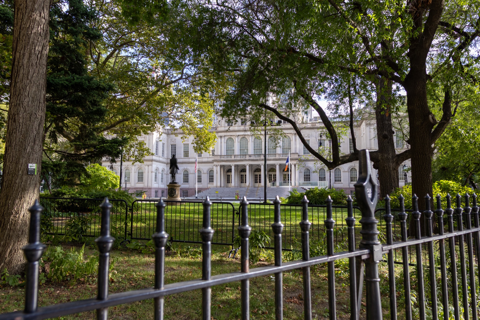 New York City Hall through the trees and iron fence of City Hall Park, September 2025.