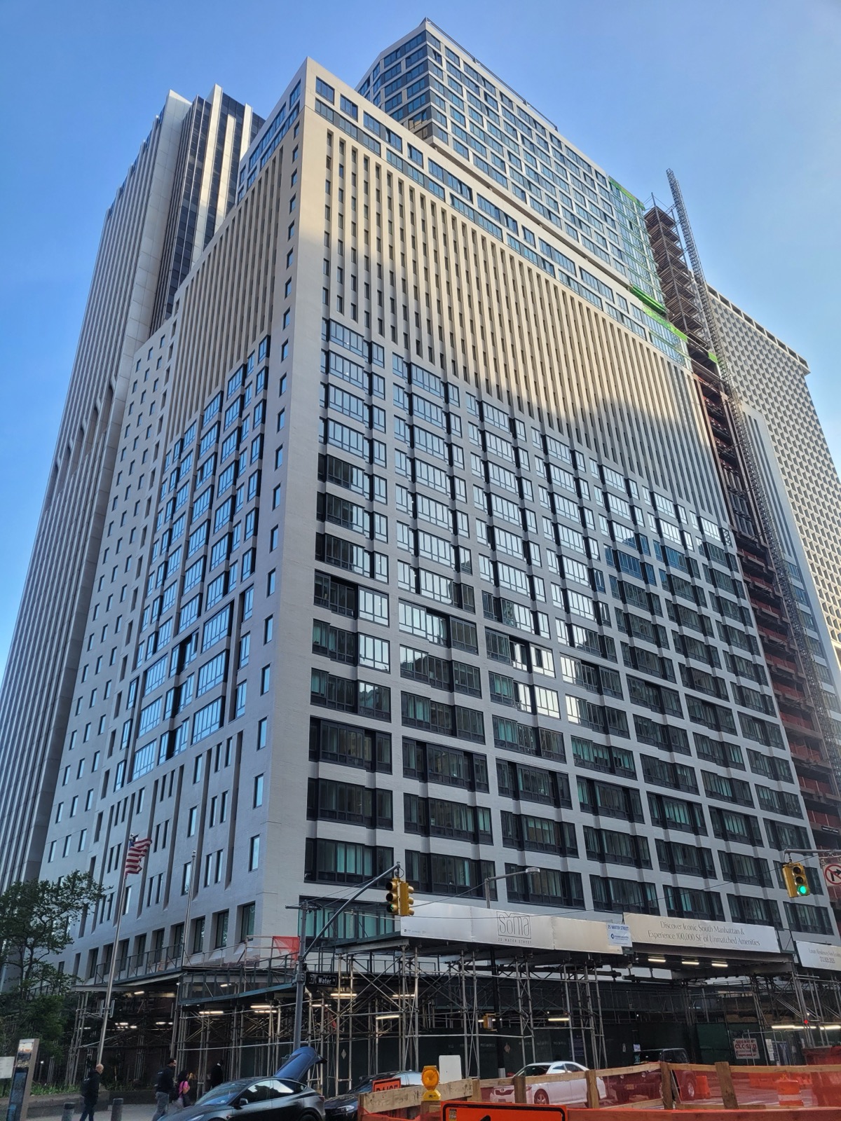 25 Water Street in May 2025 — the original 1969 frame reclad with apartment windows, the new glass floors rising on top, SoMA leasing banners over the scaffolding at street level.