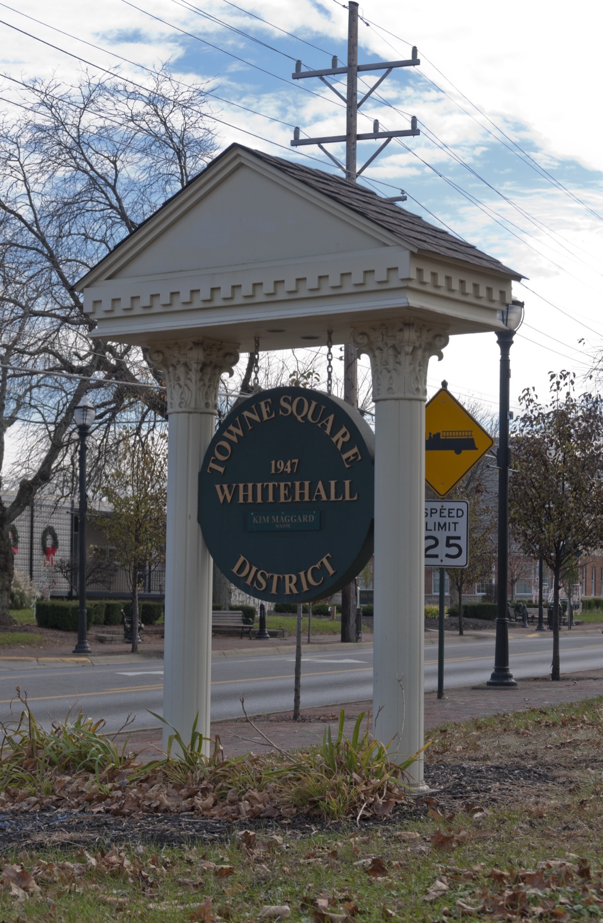 The Towne Square District sign in Whitehall, Ohio — a green medallion reading “1947 · Whitehall” under a colonnaded canopy, on a residential street.