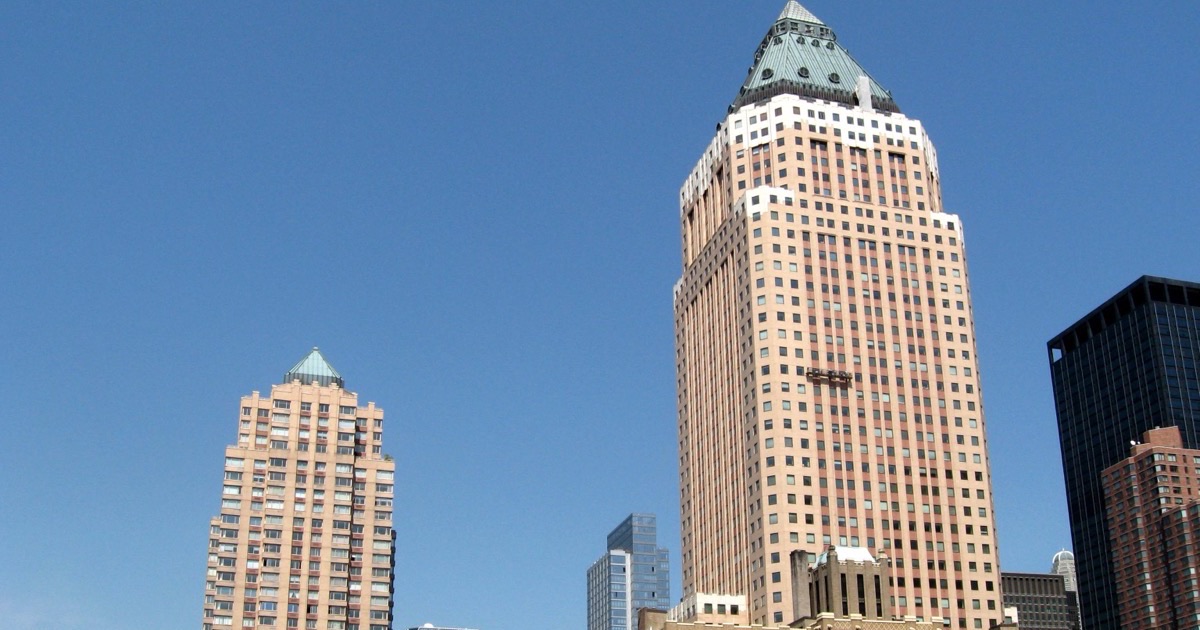 One Worldwide Plaza in Manhattan against a clear blue sky — a pink granite office tower rising to a copper pyramid crown, with a shorter residential tower of the same complex to its left.