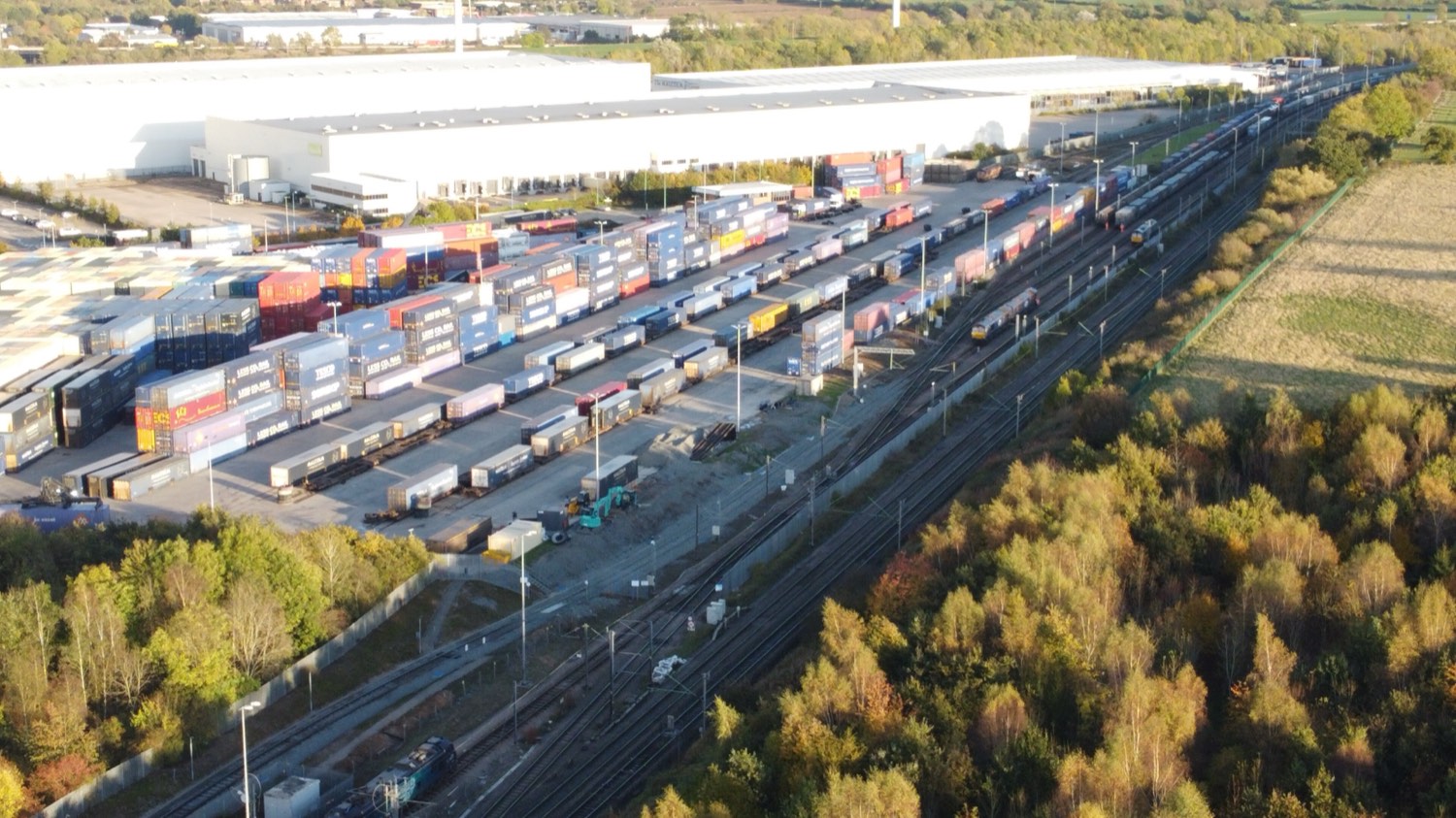Aerial view of the south yard at Daventry International Rail Freight Terminal — rows of coloured shipping containers and swap bodies on flat wagons beside rail lines, with a long white distribution warehouse behind.