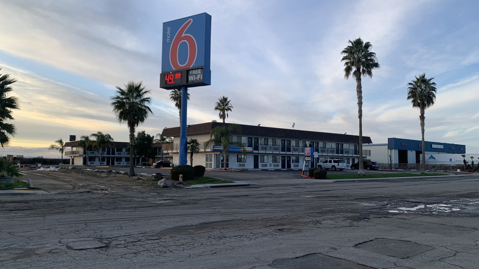 Motel 6 in Lost Hills, California at dusk — the tall red-and-blue 6 sign in front of a two-storey roadside motel lined with palm trees.