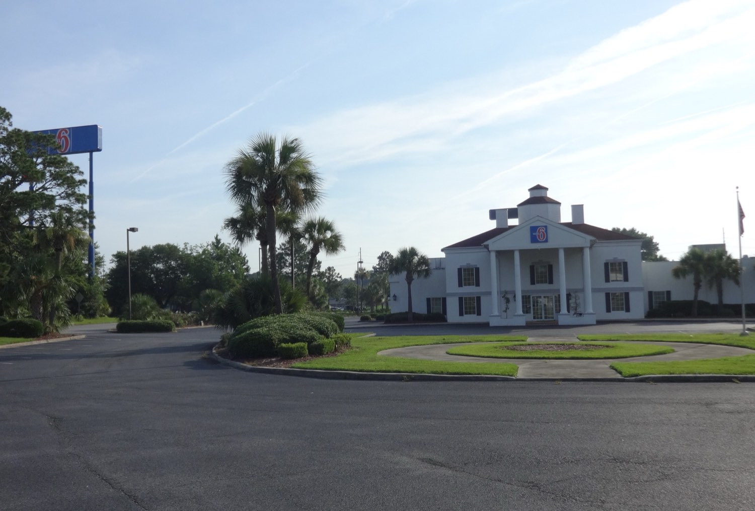 A Motel 6 in Georgia occupying a white colonial-style building with a columned portico and a cupola, its blue-and-red 6 sign on a tall pole at the roadside and palms around an empty car park.