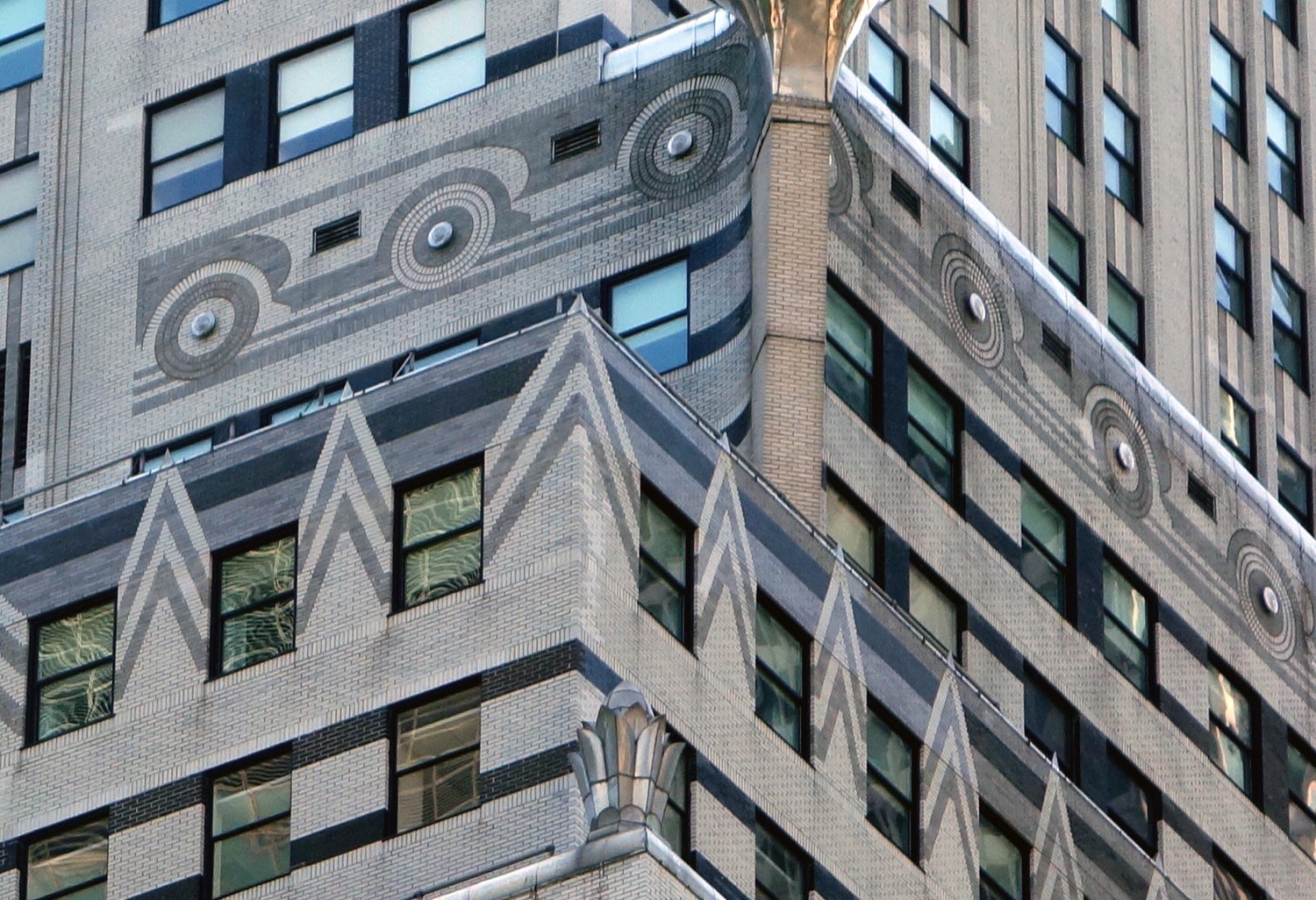 Detail of the Chrysler Building’s upper setbacks — stainless steel eagle heads projecting from the corners of the tower against a blue sky, with the Art Deco brickwork and radiator-cap ornament below.