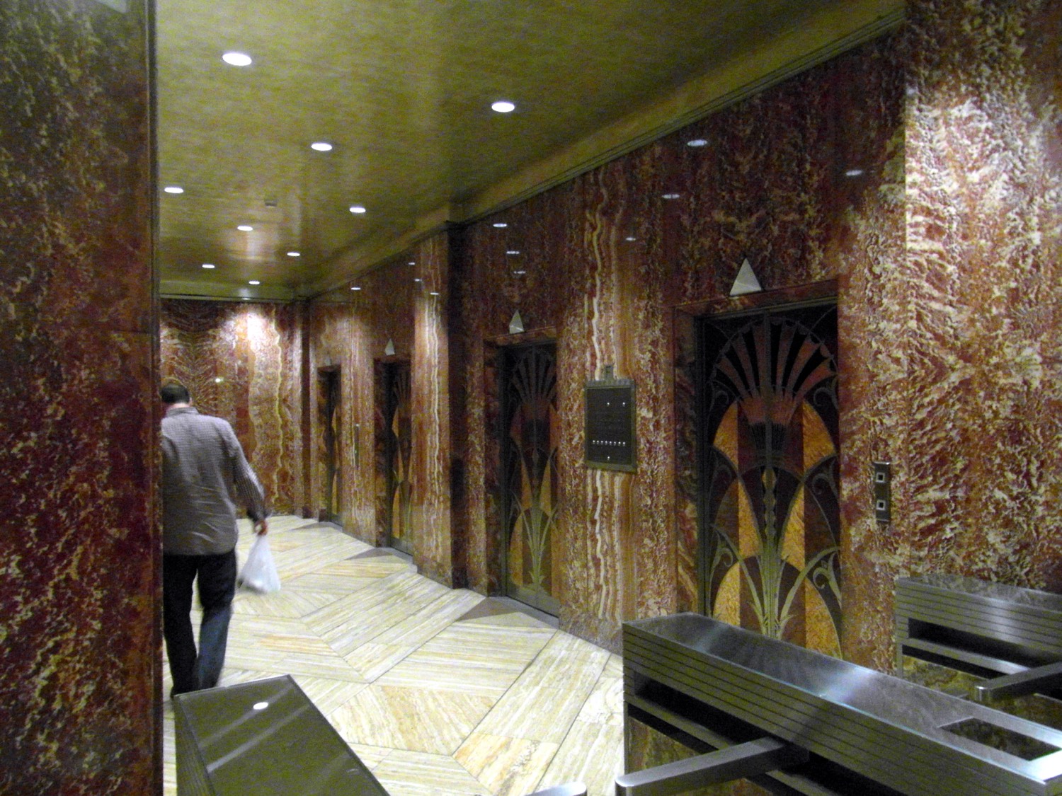 A bank of Chrysler Building elevator doors, each inlaid with a marquetry fan of wood veneers in a lotus pattern, set into the lobby’s dark marble.