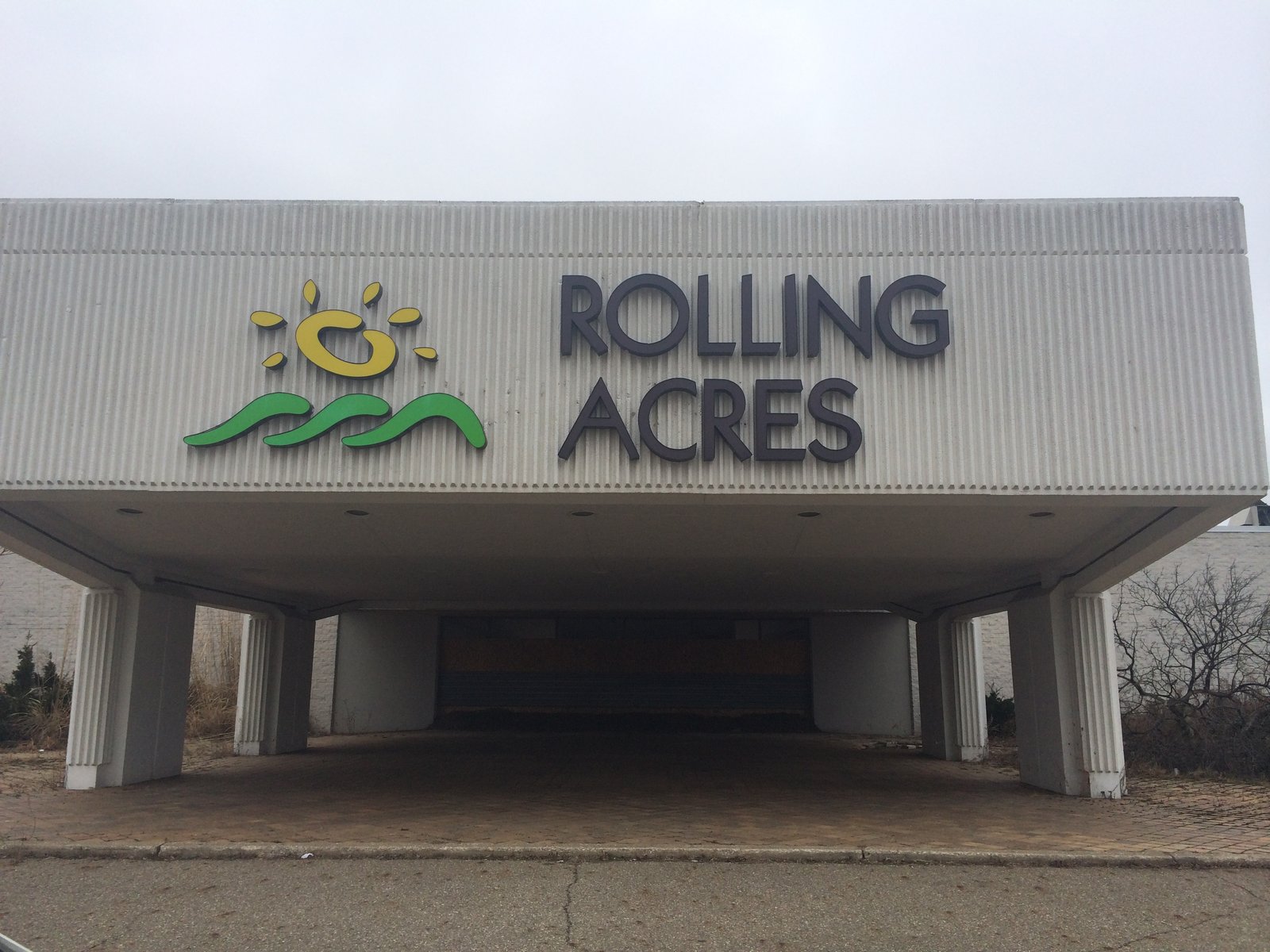 The exterior entrance of a closed shopping mall, with a “Rolling Acres” sign above an empty portico.