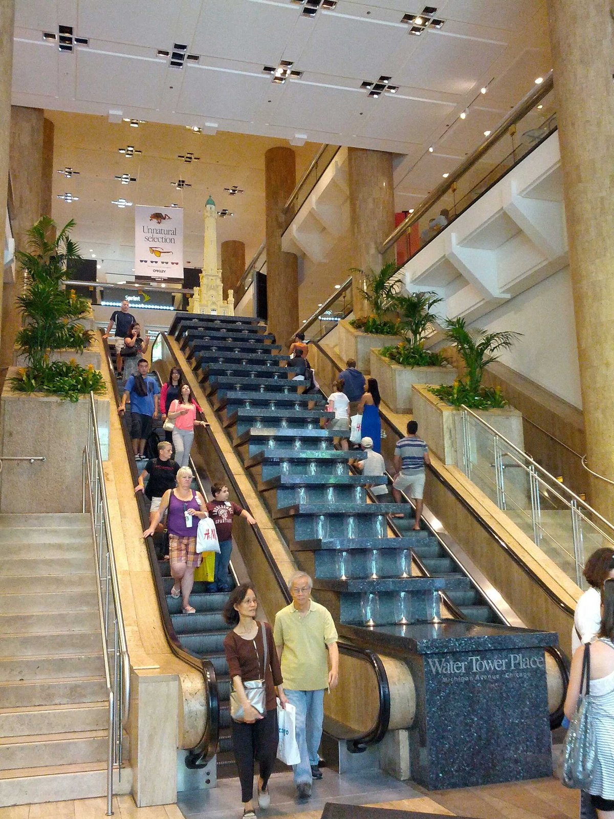 A wide terrazzo staircase and escalator rising through the multi-level atrium of Water Tower Place in Chicago, with shoppers on the stairs.