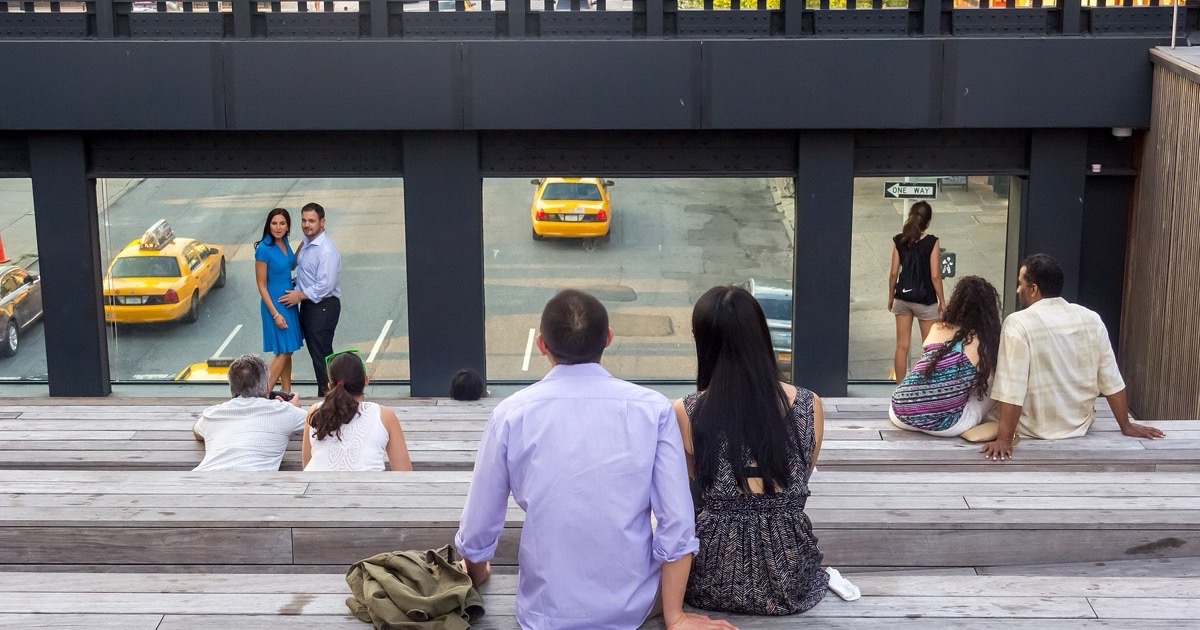 The High Line park in Manhattan — a planted walkway of grasses and perennials running between buildings, with visitors on the path and city towers rising on either side.