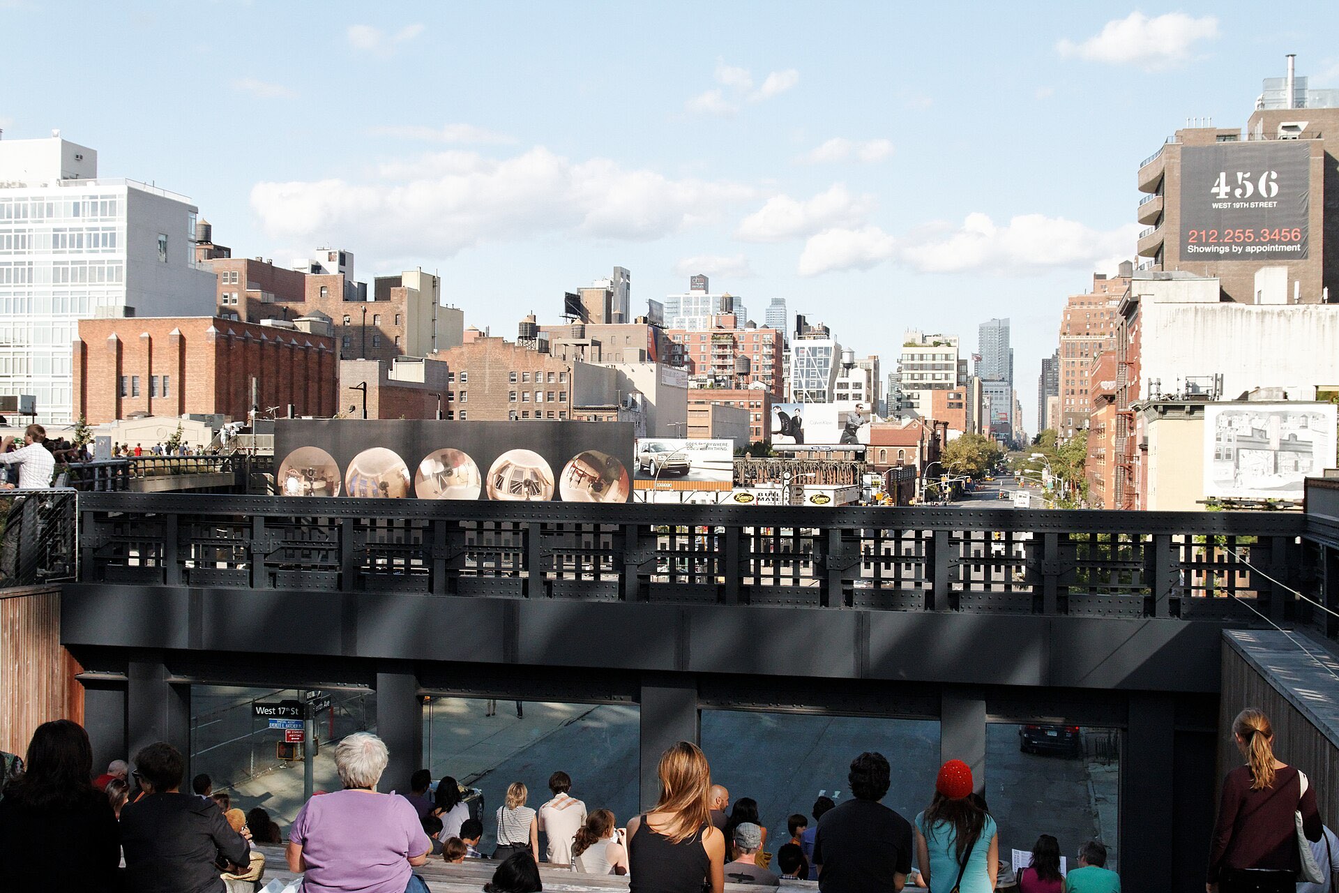The Tenth Avenue Square on the finished High Line — a sunken amphitheatre of wooden steps facing a large window that frames the avenue below, with visitors seated on the steps.