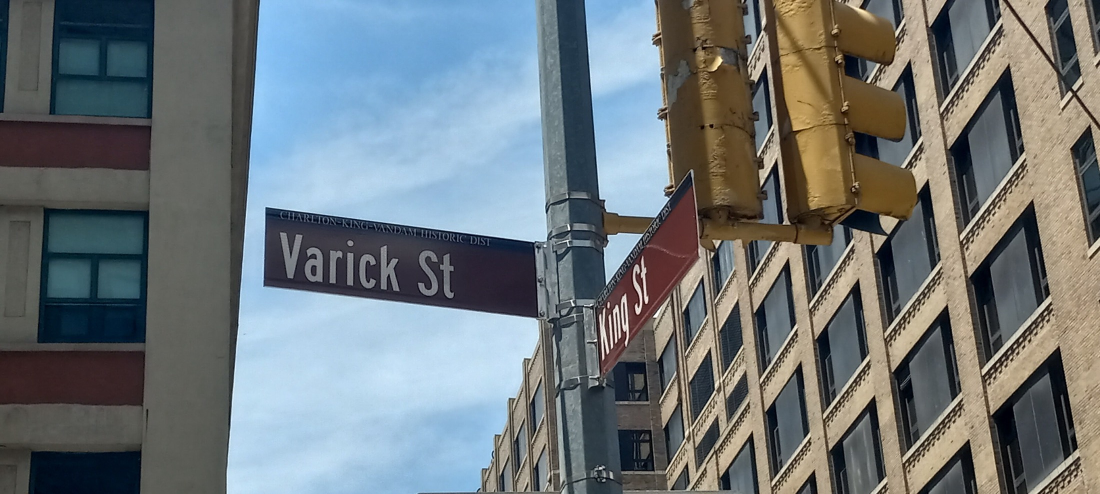 Varick Street and King Street signs, marked Charlton-King-Vandam Historic District, against the brick lofts of Hudson Square.