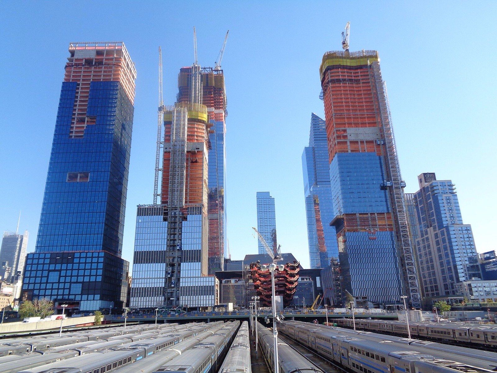 Hudson Yards towers under construction and the Vessel, seen from the High Line elevated park, with Long Island Rail Road trains parked on the yard tracks below.