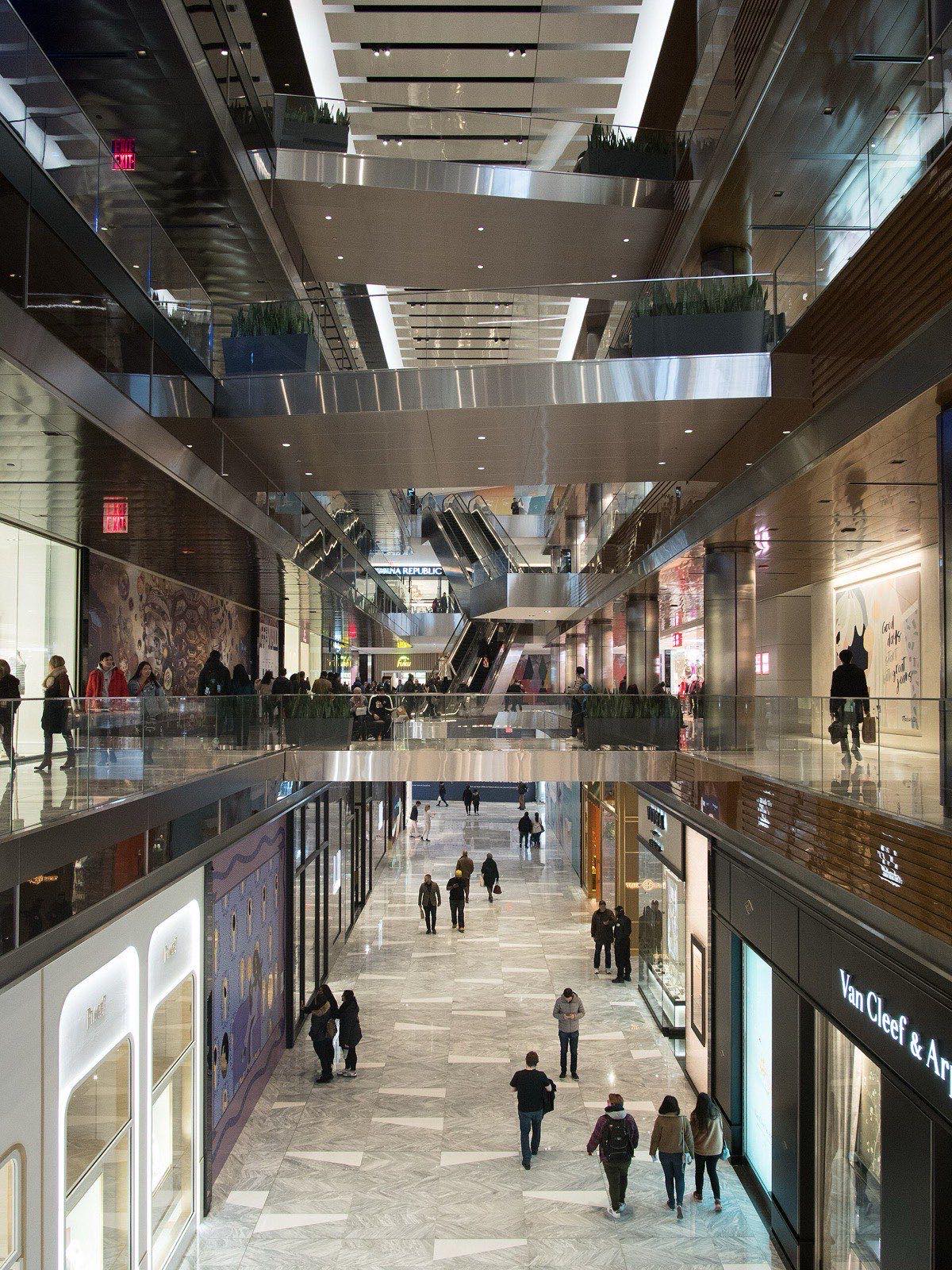 Multi-level interior atrium of The Shops and Restaurants at Hudson Yards, shoppers on a marble-floored corridor lined with storefronts.