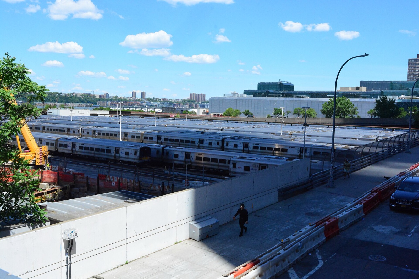 The open, uncovered stretch of the West Side rail yard seen from the High Line — rows of parked commuter trains, the Javits Center, and the Hudson River shoreline beyond.