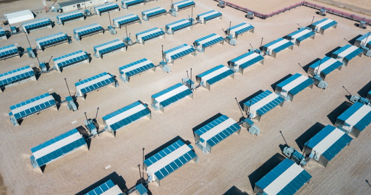 Aerial view of Hut 8’s bitcoin mining campus: rows of blue-roofed mining containers on gravel, receding in ranks across the site.