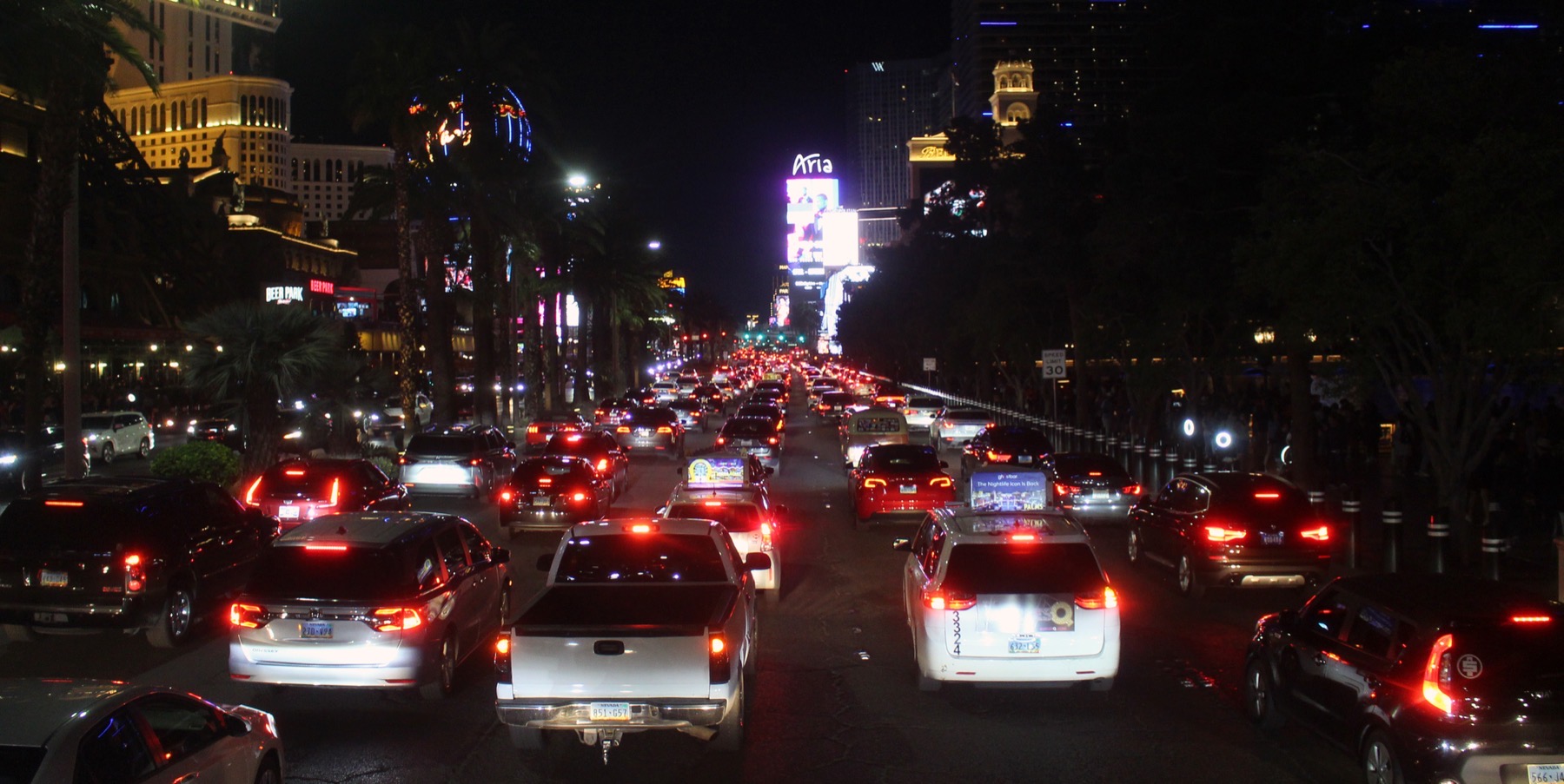 Southbound Las Vegas Boulevard at night, jammed with brake-lit traffic in front of the Bellagio, with Strip towers lit up in the distance.