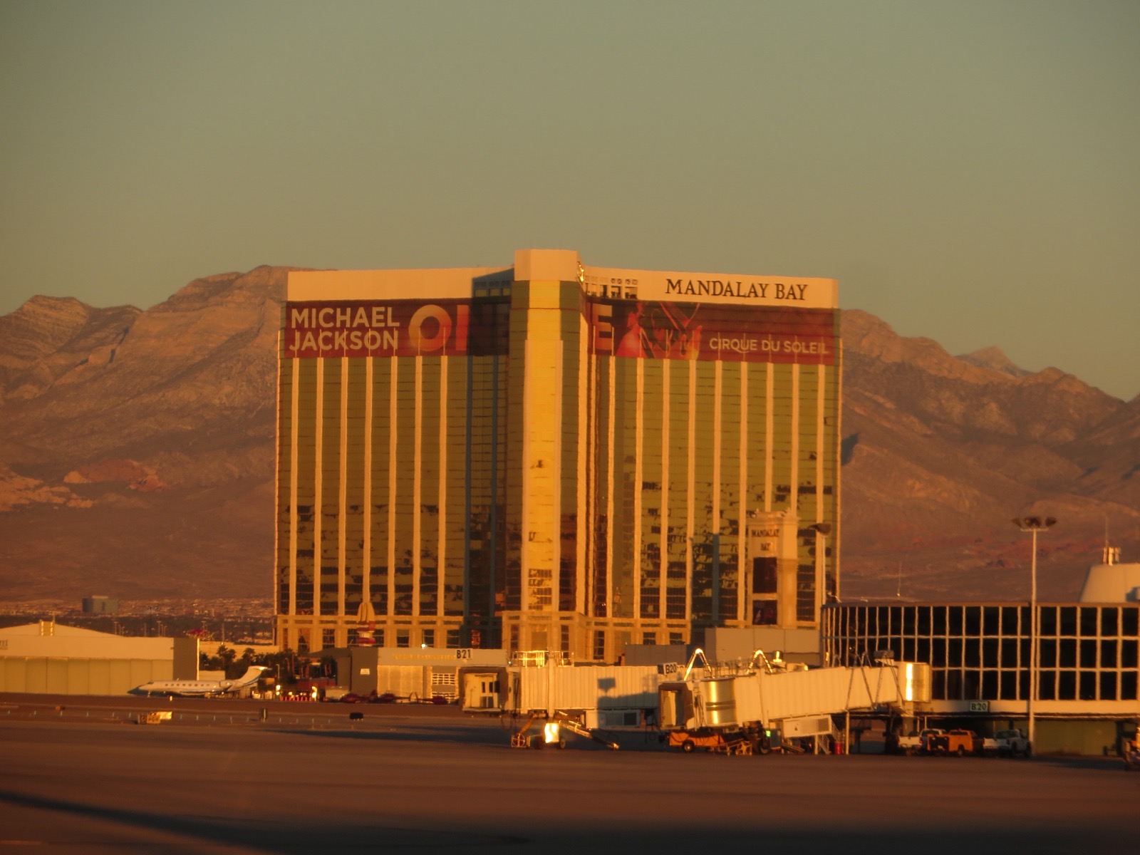 Mandalay Bay’s gold-glass tower at sunset with its lettering visible, photographed from the airport tarmac with the Spring Mountains behind.