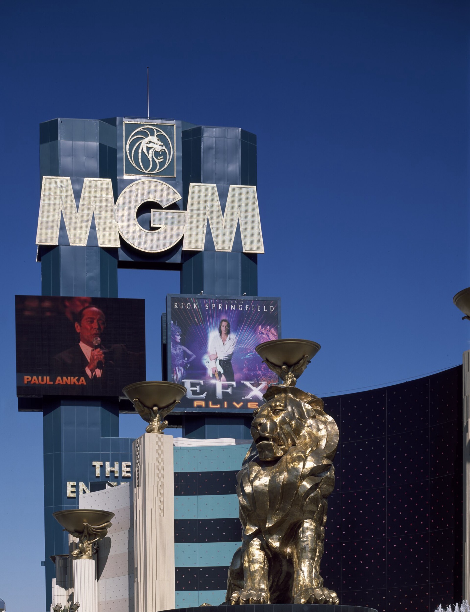 The MGM Grand’s dark green-glass tower with its illuminated MGM lettering and lion medallion, and the bronze lion statue in the foreground.