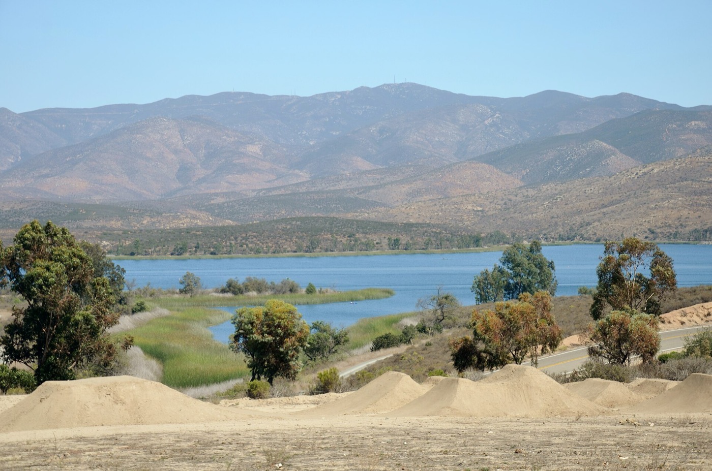 Bare, freshly graded dirt mounds in the foreground with a reservoir and dry hills behind, in the EastLake area of Chula Vista.