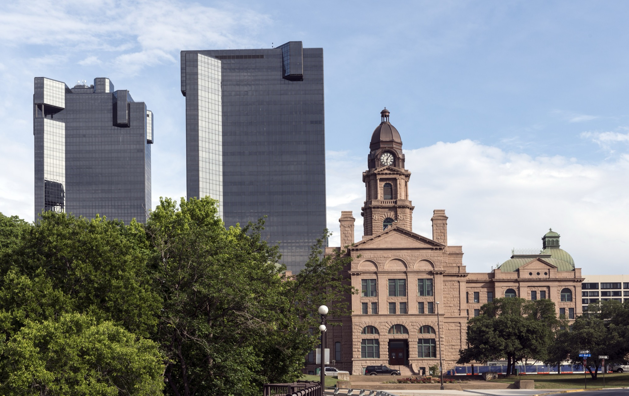 The 1895 Tarrant County Courthouse in Fort Worth — pink granite, clock tower and copper dome — framed against two black-glass office towers.