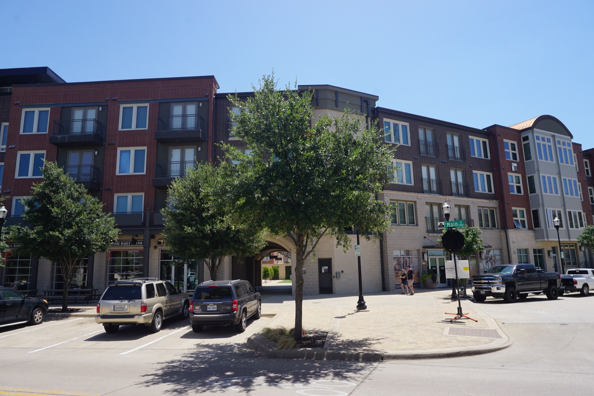 Union at Carrollton Square, a four-story brick apartment block with ground-floor retail in downtown Carrollton, Texas, under a clear summer sky.