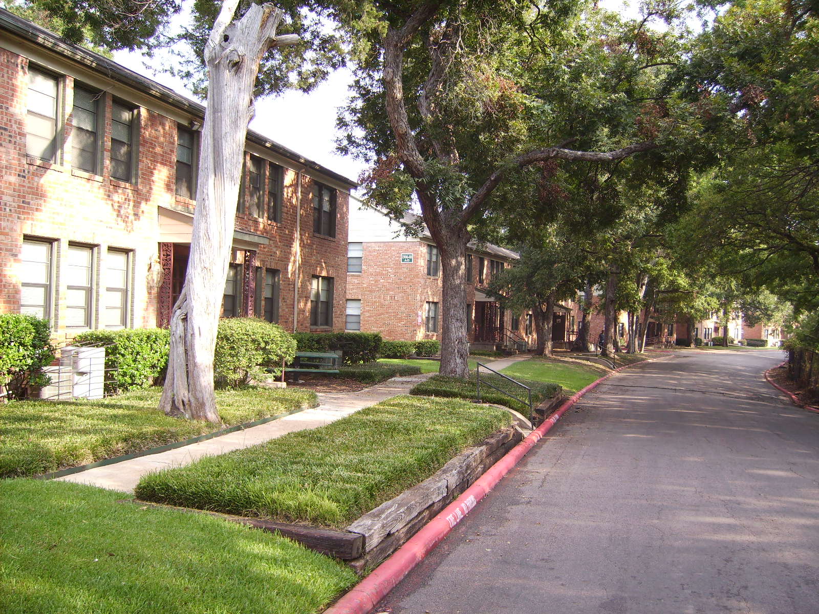 Wynnewood Parks, a two-story brick garden-apartment complex on Zang Avenue in Oak Cliff, Dallas — lawns, mature trees and a curbed private drive.