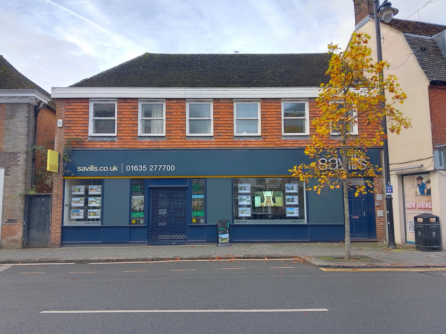 A Savills estate agency storefront in Newbury, England — the firm’s yellow-on-navy branding above a Georgian-style shopfront window.