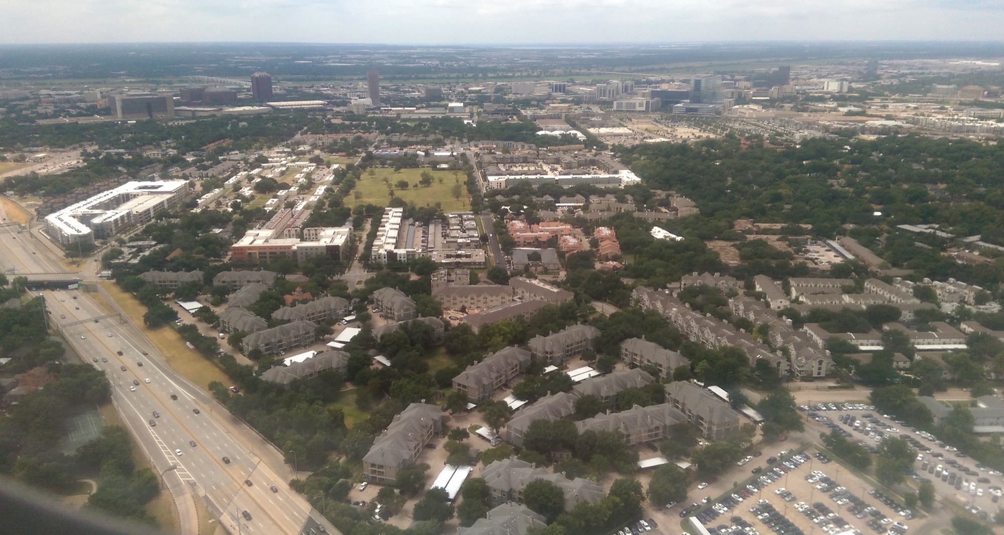 An aerial view over Dallas, Texas: clusters of garden-style apartment complexes beside a highway, photographed from a plane window.