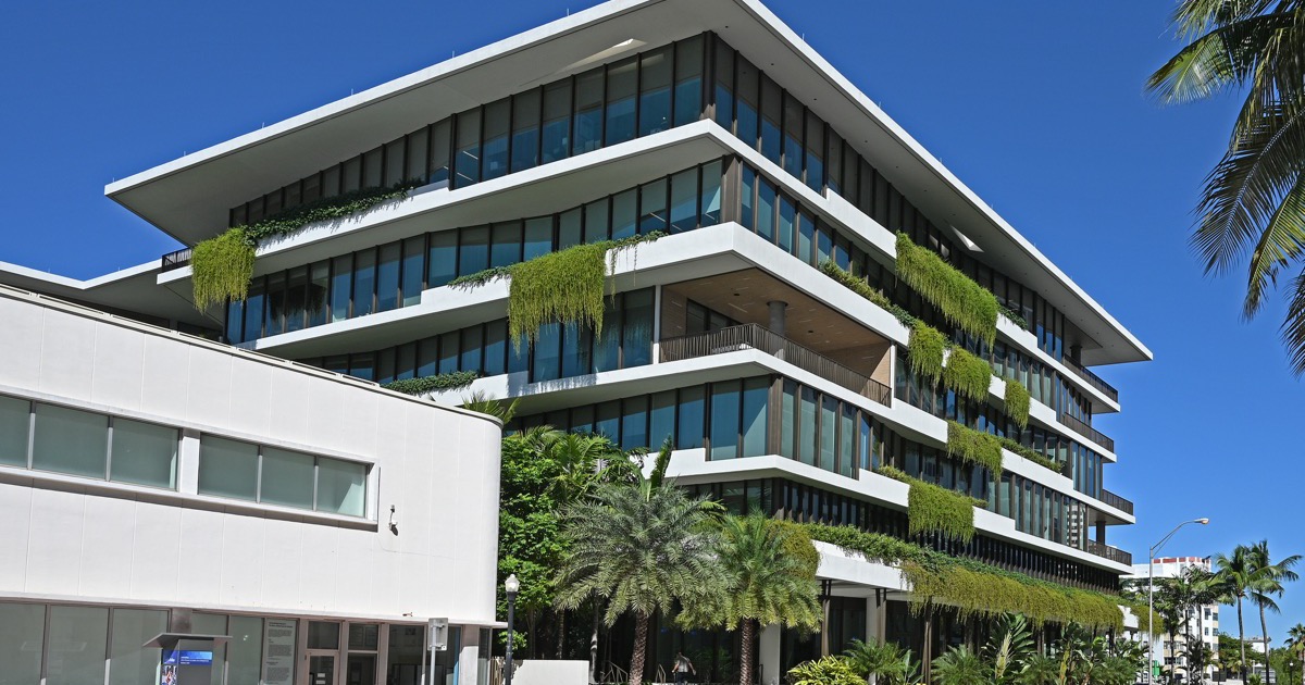 Starwood Capital Group’s headquarters at 2340 Collins Avenue, Miami Beach — a white terraced office building with cascading greenery and palm trees under a deep blue sky.