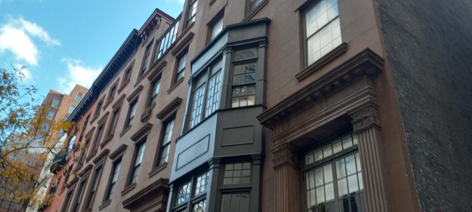 A row of 19th-century brownstone rowhouses near Gramercy Park, Manhattan, with bay windows, carved stone lintels, and autumn leaves on a tree in the foreground.