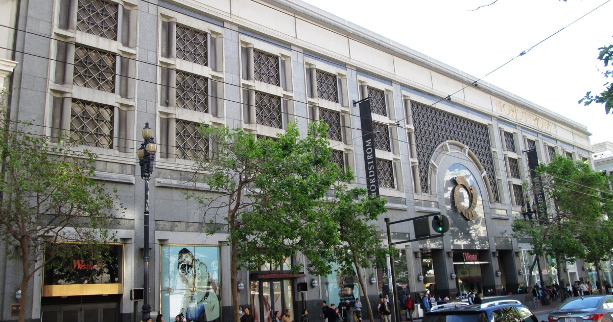 The Westfield San Francisco Centre on Market Street in 2017 — a granite and glass facade with gold NORDSTROM lettering and hanging banners, busy with pedestrians and traffic.