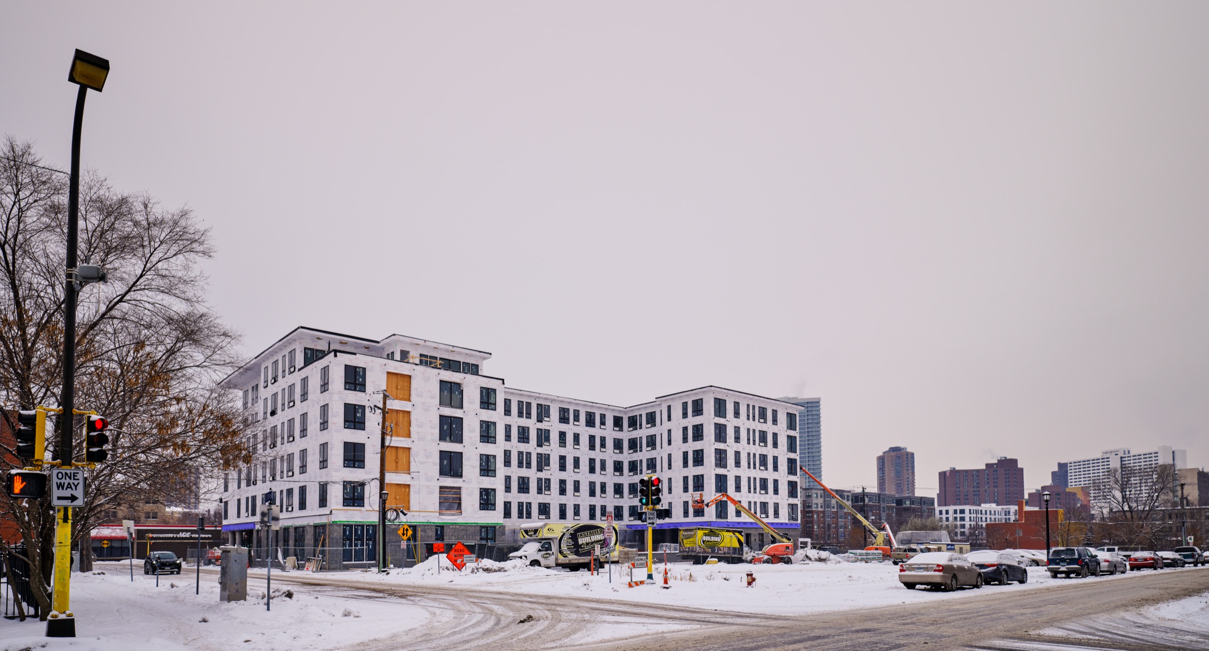 A large wood-frame apartment building under construction in winter, Minneapolis — a near-complete five-story block in the snow, construction equipment at its base, the skyline behind.
