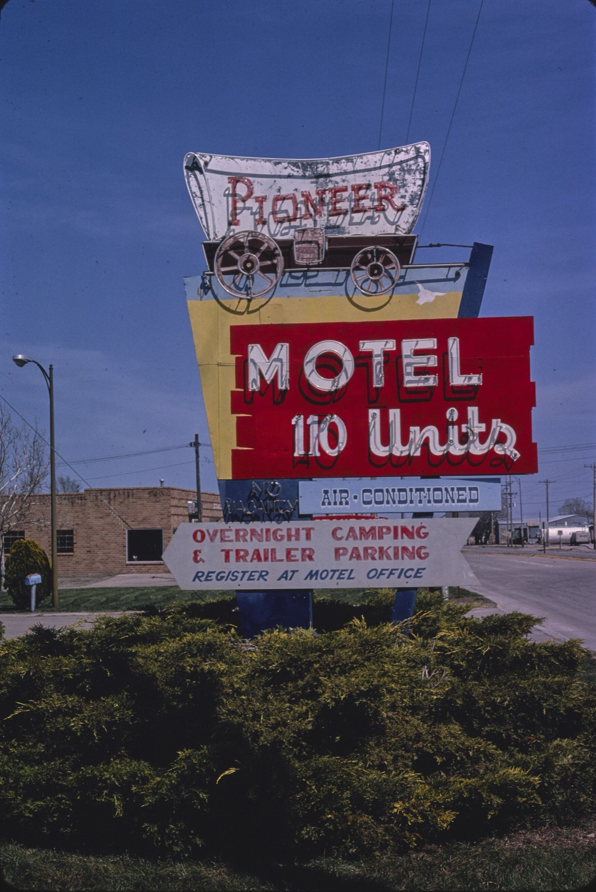 A tall neon roadside motel sign in Minden, Nebraska, shaped like a covered wagon, reading PIONEER MOTEL, 110 UNITS, AIR-CONDITIONED, OVERNIGHT CAMPING AND TRAILER PARKING, photographed against a blue sky.