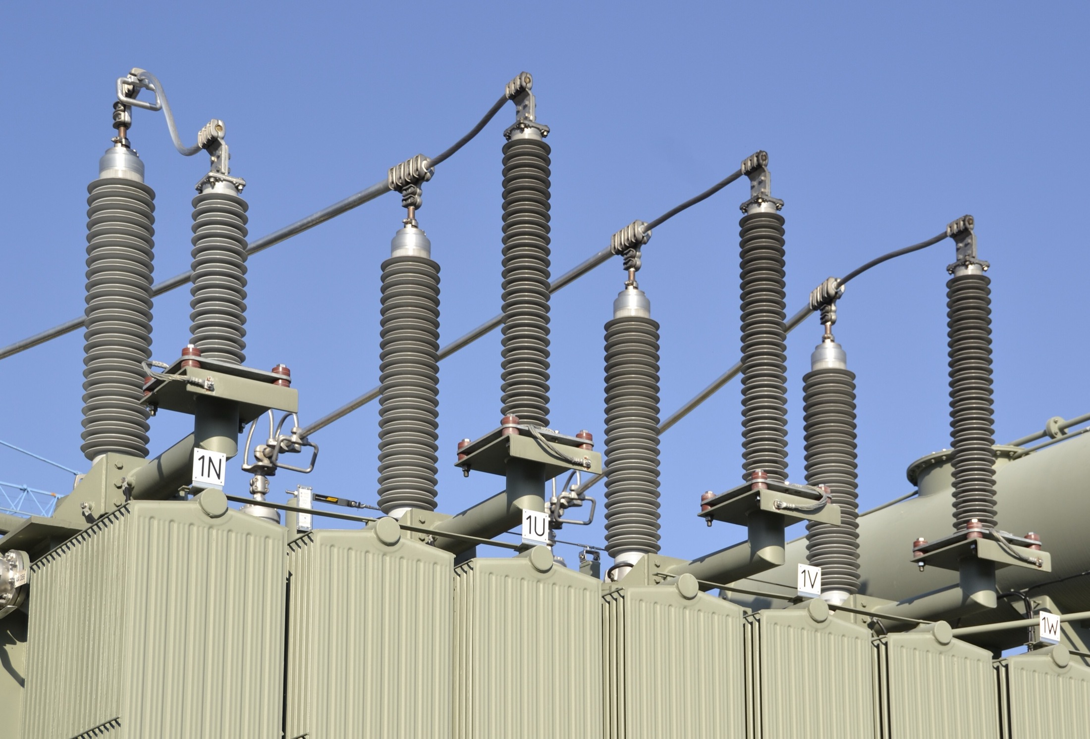 High-voltage bushings rising from a large power transformer against a blue sky.
