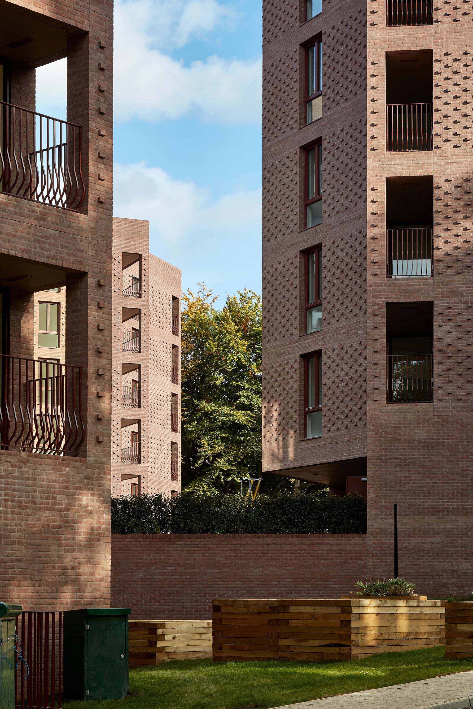Brick apartment buildings and corner balconies frame a planted courtyard at Lion Green Road.